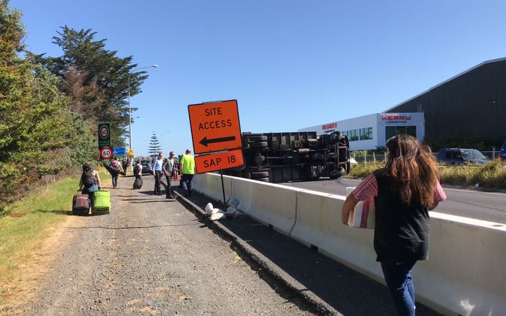The second truck can be seen on its side, and people can be seen out of their cars wheeling suitcases towards Auckland Airport. Photo: RNZ / Jeremy Brick http://www.radionz.co.nz/news/national/320905/truck-crashes-delay-traffic-to-auckland-airport